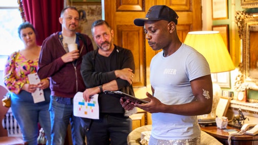 A poet reading surrounded by an audience inside a highly decorated room at Hatchlands Park